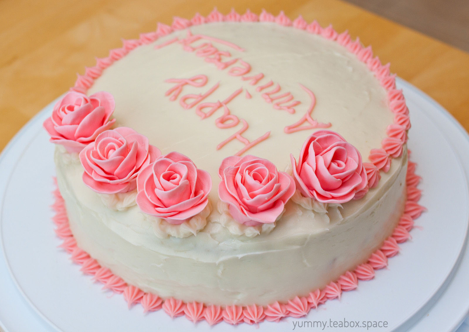 Closer view of five pink roses on a round white cake.
