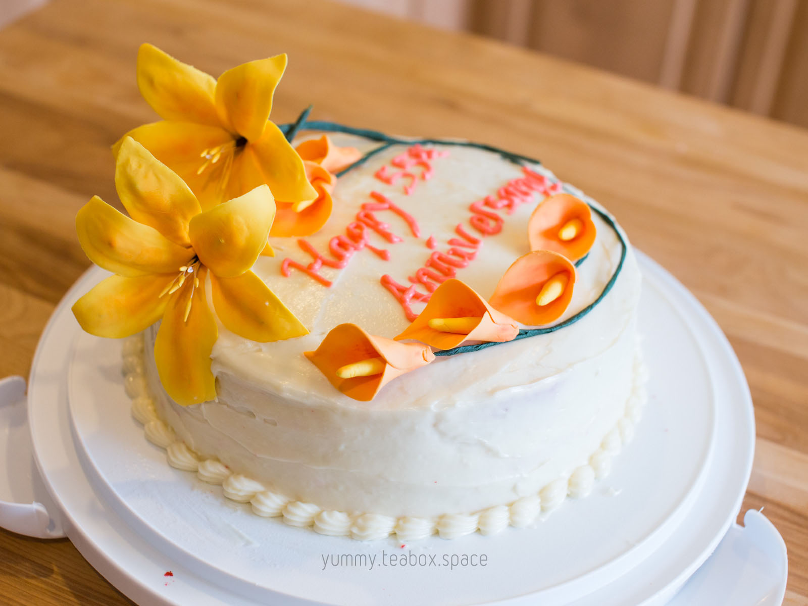 Round cake with white frosting and decorated with yellow lilies and orange calla lilies.