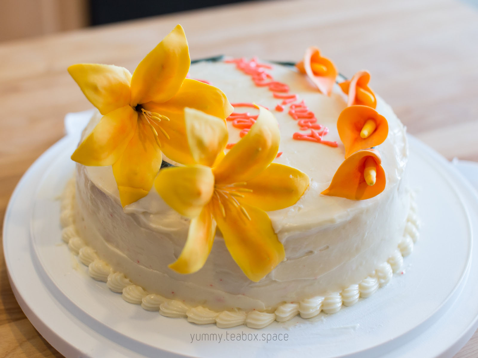 Round cake with white frosting and decorated with yellow lilies and orange calla lilies.
