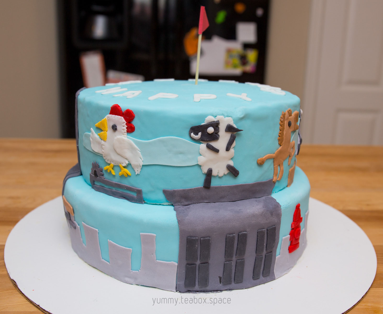 2-tier blue cake with images of chicken, sheep, and horse from Ultimate Chicken Horse on the side.