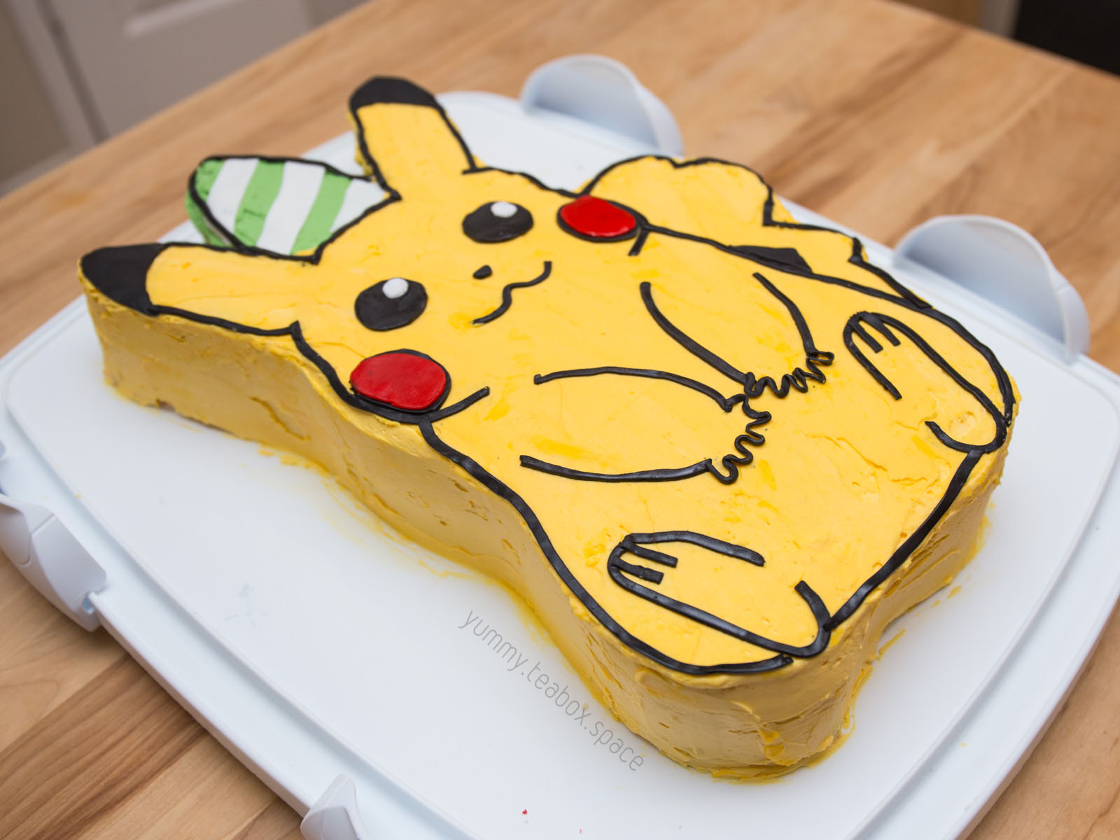 Cake that looks like a sitting Pikachu with a party hat.