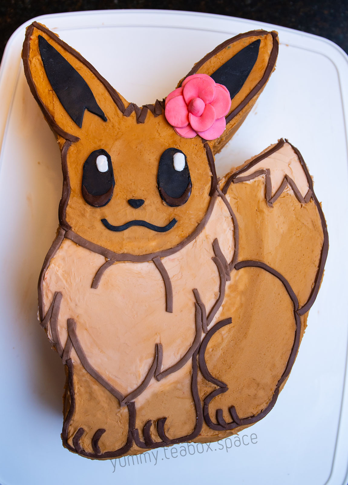 Cake that looks like the Pokemon Eevee with a pink flower on the ear