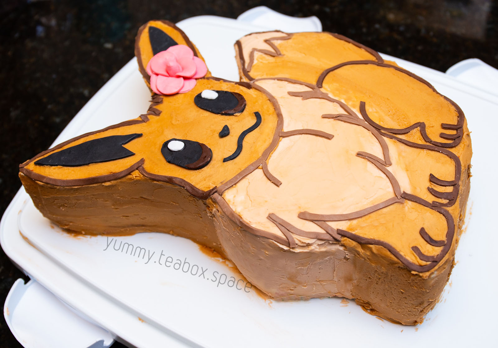 Cake that looks like the Pokemon Eevee with a pink flower on the ear